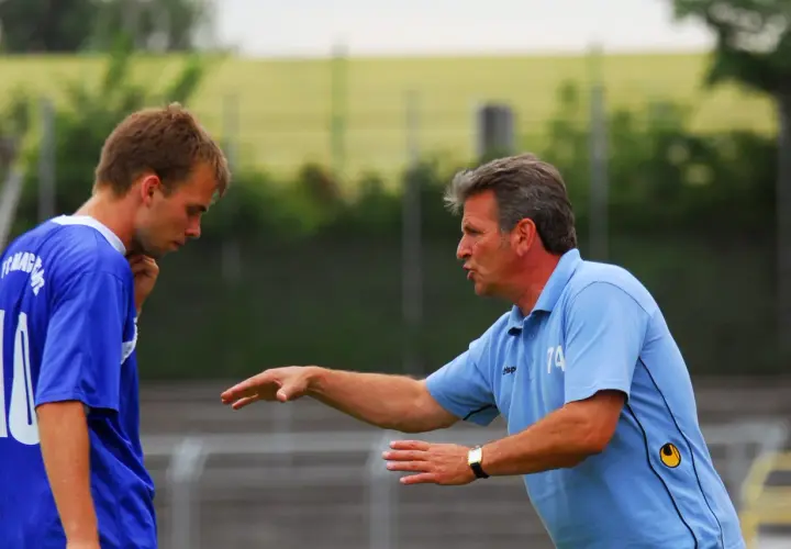 Trainer Martin Hoffmann gibt einem Spieler Anweisungen auf dem Fußballplatz.