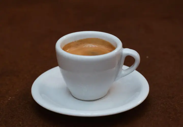 Ein weißer Becher mit cremigem, doppeltem Espresso steht auf einer Untertasse.