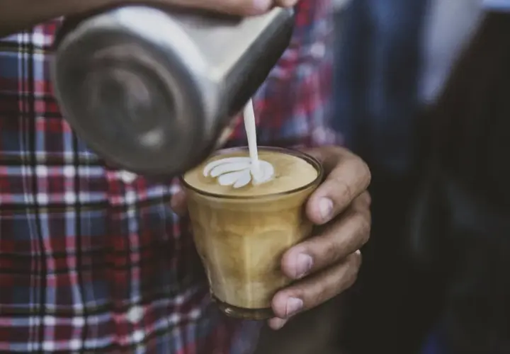 Barista wylewa mleko z dzbanka, tworząc wzór na kawie. To właśnie zabielacz do kawy, który nadaje jej kremową konsystencję i piękny wygląd.