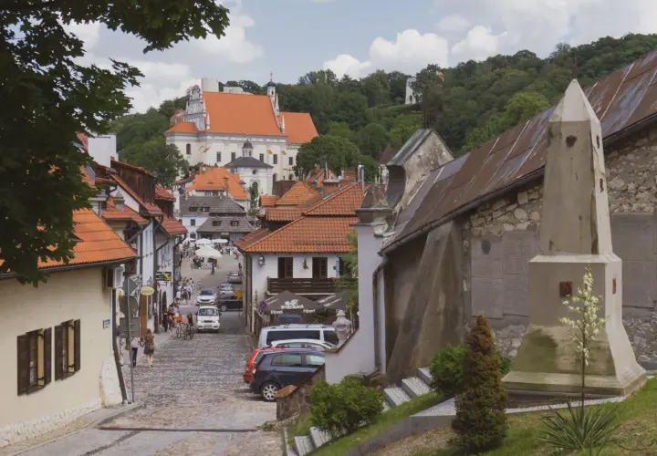 Ulica w Kazimierzu Dolnym z widokiem na kościół i wzgórza. Widać kamienne domy, brukowaną drogę i turystów. Kazimierz Dolny atrakcje zachwycają.