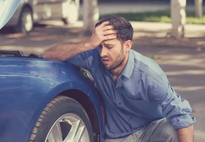 Hombre frustrado con el capó abierto de su coche azul. A veces, merece la pena arreglar un coche de 20 años.