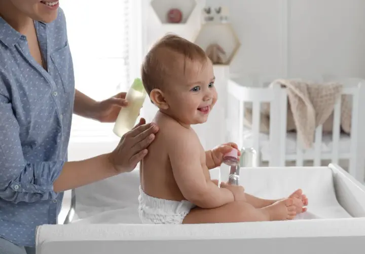 Mama delikatnie wmasowuje w plecy dziecka olejek migdałowy do kąpieli. Uśmiechnięty maluch trzyma buteleczkę z płynem.