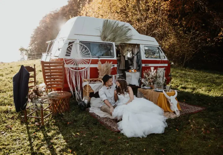 Un couple en tenue de mariage profite d'un mariage pique-nique champêtre près d'un van aménagé, décoré de style bohème.