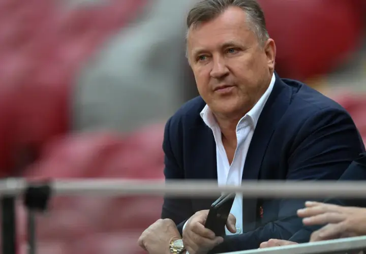 Prezes PZPN w garniturze, z telefonem w dłoni, siedzi na trybunach stadionu.