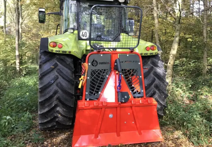 Ein grüner Traktor mit einer roten Forstseilwinde im Wald. Die Seilwinde ist bereit für den Einsatz, um Holz zu ziehen.