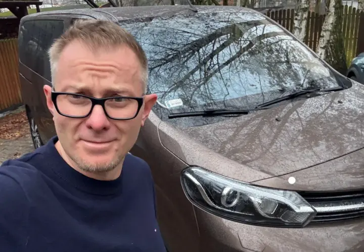 Mężczyzna w okularach przed brązowym vanem, gotowy do podpisania umowy komisu.