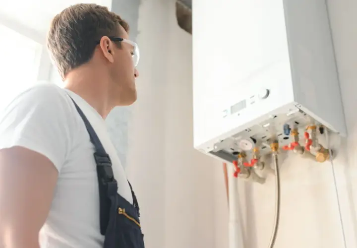 Technik w okularach ochronnych sprawdza instalację gazową. Wykonuje odpowietrzanie pieca gazowego, dbając o jego prawidłowe działanie.