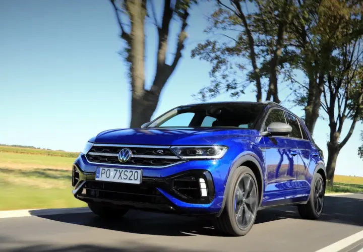Niebieski Volkswagen T-Roc R pędzi po wiejskiej drodze, otoczony drzewami i polami.