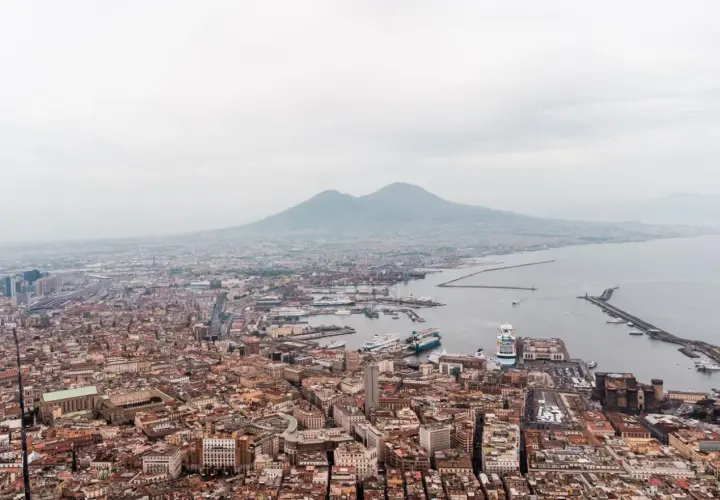 Panoramic view of Napoli, Naples, with Mount Vesuvius looming in the distance over the bustling port and city.
