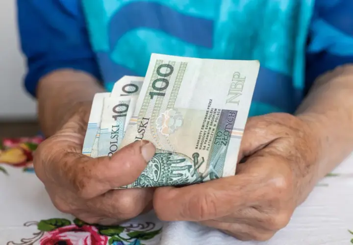 Dłonie trzymają polskie banknoty. Może to symbolizować emeryturę za medal olimpijski, zapewniającą godne życie.