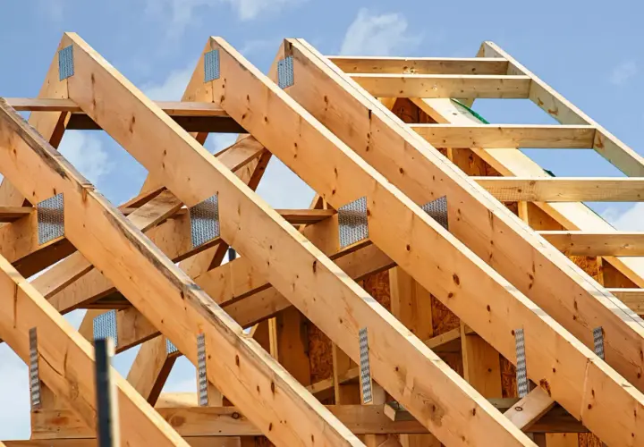 Structure en bois d'une charpente simple, avec des poutres assemblées par des équerres métalliques sous un ciel bleu.