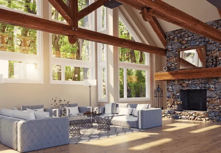 Vaste salon avec cheminée en pierre et un impressionnant plafond cathédrale bois. De grandes fenêtres donnent sur une forêt luxuriante.