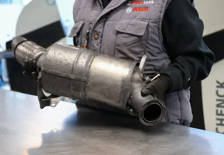 Mechanik w rękawiczkach trzyma metalowy element układu wydechowego samochodu.