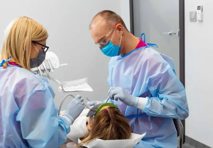 Znieczulenie u dentysty w ciąży. Dwoje stomatologów w fartuchach i maskach wykonuje zabieg u pacjentki.