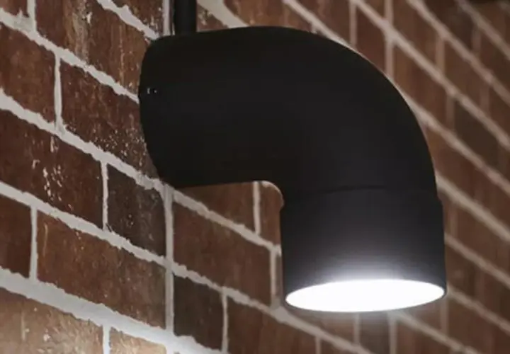 Applique fai da te in metallo nero a forma di gomito, illumina una parete in mattoni rossi.