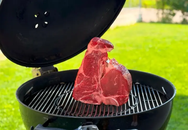 Una succulenta bistecca alla fiorentina cruda riposa sulla griglia di un barbecue, pronta per essere cucinata all'aperto.