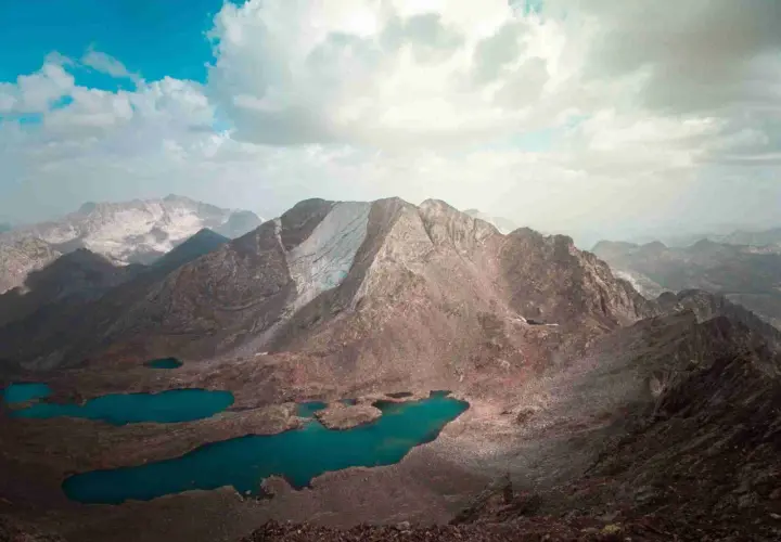 Paisaje montañoso con lagos turquesa, como si fueran los picos del infierno. Nubes blancas y cielo azul.