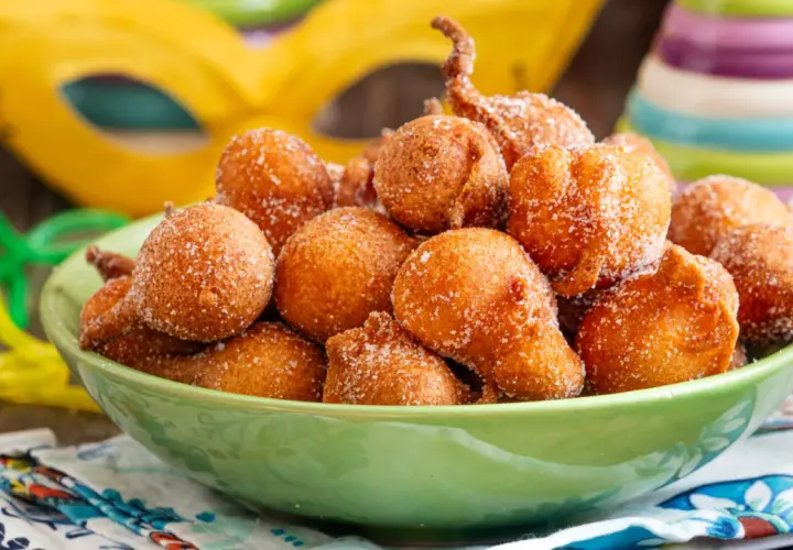 Frittelle di una volta, dolcetti dorati cosparsi di zucchero, pronti per il Carnevale. Maschere e coriandoli sullo sfondo.