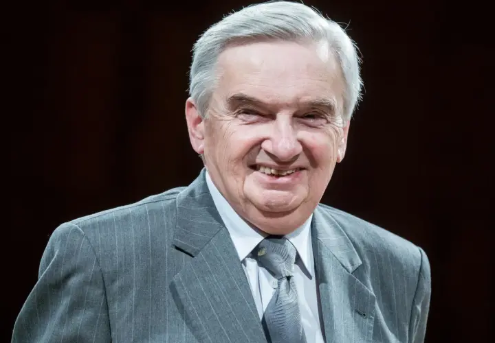 Uśmiechnięty starszy pan w szarym garniturze. Trudno zgadnąć, ile lat ma sznuk, ale wygląda na doświadczonego i życzliwego.