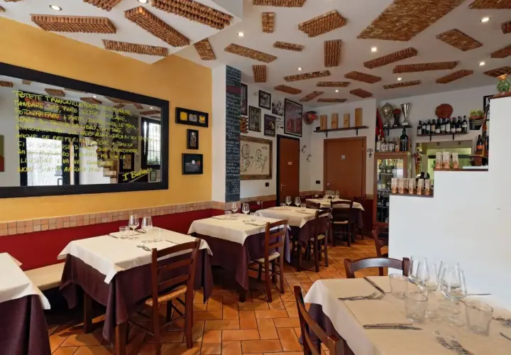 Interno di un'accogliente osteria a Bologna, con tavoli apparecchiati e un soffitto decorato con tappi di sughero.