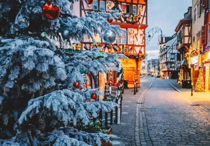Verschneiter Weihnachtsbaum mit roten Kugeln vor Fachwerkhäusern, die mit Lichtern geschmückt sind. Perfekte reiseziele winter.
