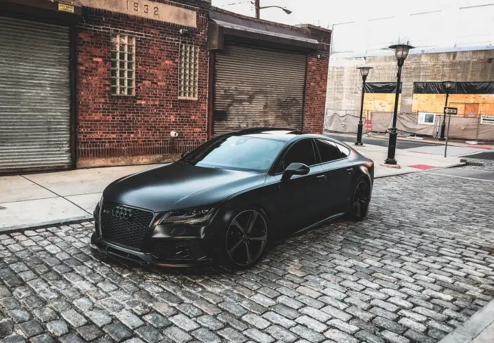 Matowy czarny Audi RS7 na brukowanej ulicy przed ceglanym budynkiem.