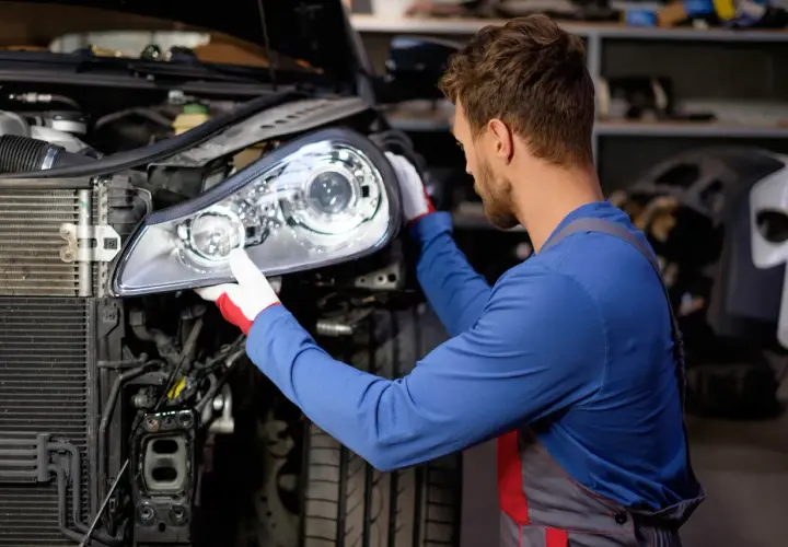 Mecánico con guantes blancos y rojos instalando un faro nuevo en un coche.