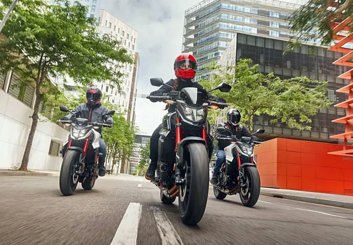 Tres motociclistas con cascos circulan en fila por una calle urbana. Una motocicleta puede circular por el arcén, ofreciendo agilidad entre el tráfico.