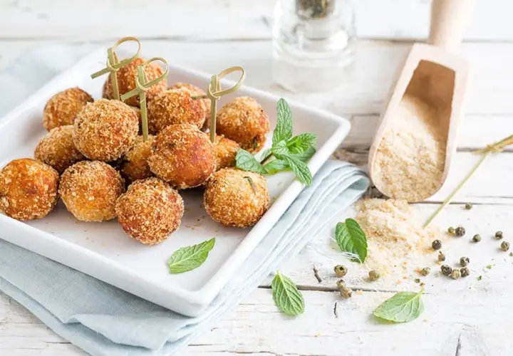 Deliziose polpette tonno e ricotta, dorate e croccanti, servite su un piatto bianco con menta fresca.