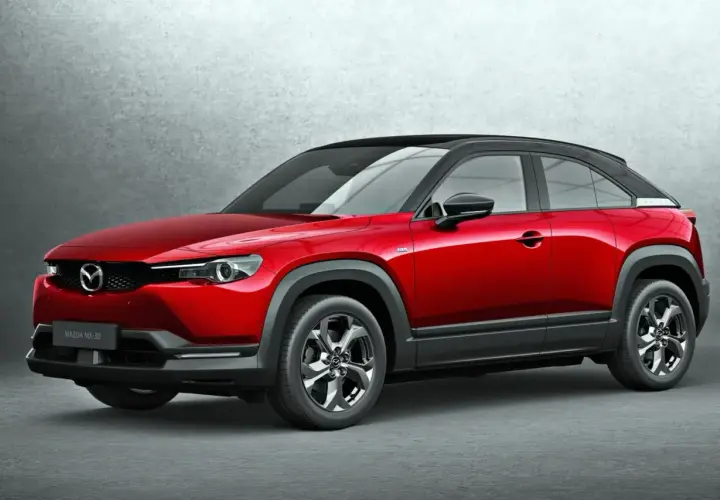 Czerwona Mazda MX-30 z czarnym dachem, stojąca na tle szarej ściany. Stylowy crossover miejski.