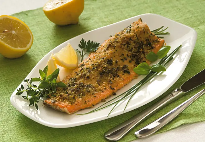 Deliziosa trota salmonata al forno, croccante e profumata, servita con limone e erbe aromatiche fresche.