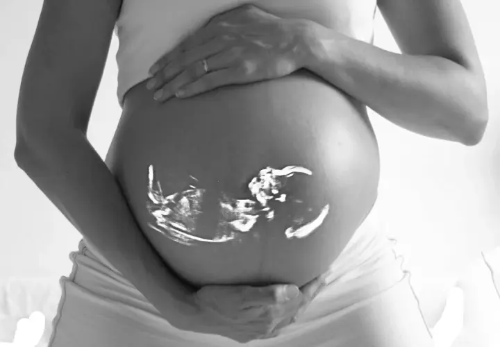 Gravid vecka 6 ultraljud projicerat på en gravid mage. En hand vilar på magen, en ring syns på fingret.