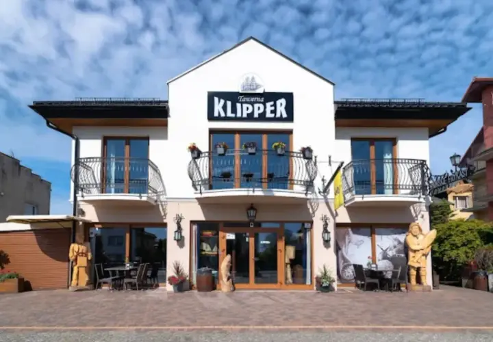 Tawerna "Klipper" we Władysławowie z drewnianymi rzeźbami i stolikami na zewnątrz.