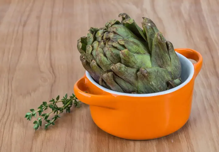Un gros artichaut vert prêt pour la cuisson Cookeo, avec une branche de thym frais à côté.