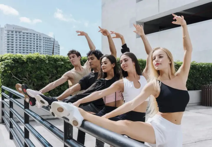 Giovani ballerini in una lezione di danza all'aperto, con un edificio moderno e vegetazione sullo sfondo.