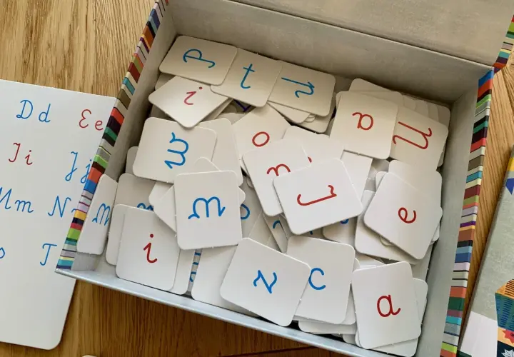 Pudełko z kartami do nauki liter, obok tablica z zapisanymi literami.