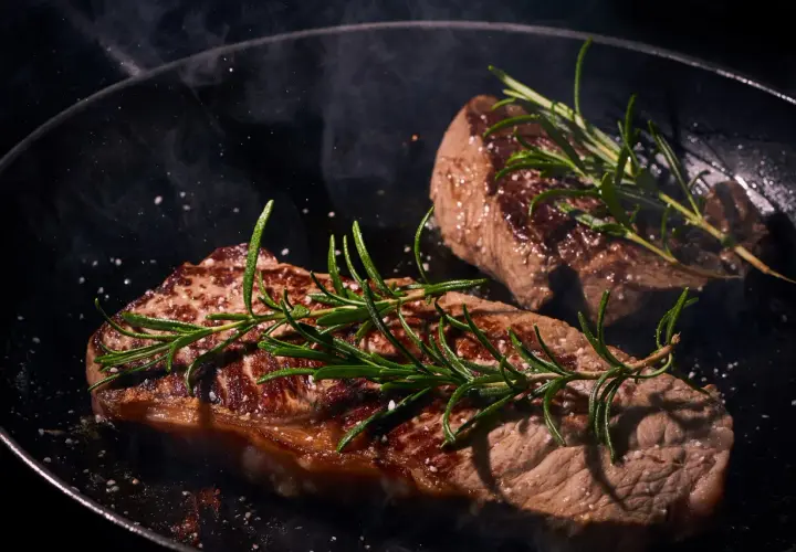 Deux steaks de vache Black Angus savoureux mijotent dans une poêle, ornés de romarin frais et de gros sel.