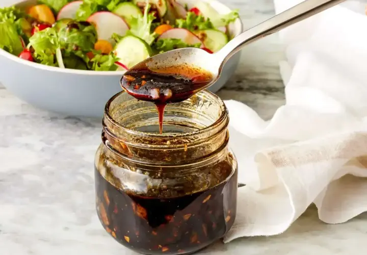Łyżka polewa sałatkę gęstym, ciemnym sosem balsamicznym z słoiczka.