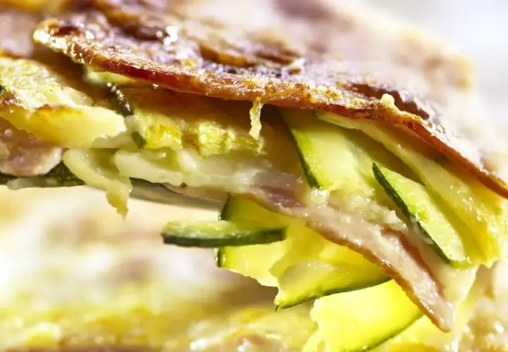 Una fetta di parmigiana di zucchine bianca, con strati di zucchine, formaggio filante e una crosticina dorata.