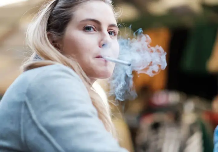 Ragazza bionda con sigaretta tra le labbra, fumo denso che le avvolge il viso. Un momento di pausa, forse dopo essersi lavata i denti, per fumare.