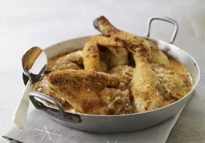 Un plat de poulet Gaston Gérard gratiné, doré et croustillant, servi dans un plat en métal avec une cuillère.