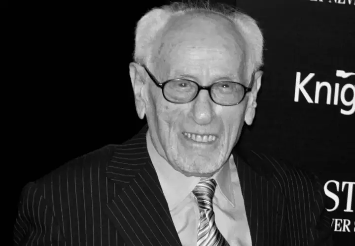Eli Wallach, w okularach i garniturze w prążki, uśmiecha się. Ikona kina, pamiętana z niezapomnianych ról w filmach.