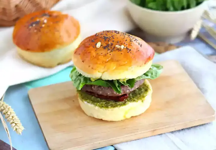 Pyszny burger włoski z soczystym mięsem, świeżą sałatą i aromatycznym pesto na złocistej bułce z makiem.