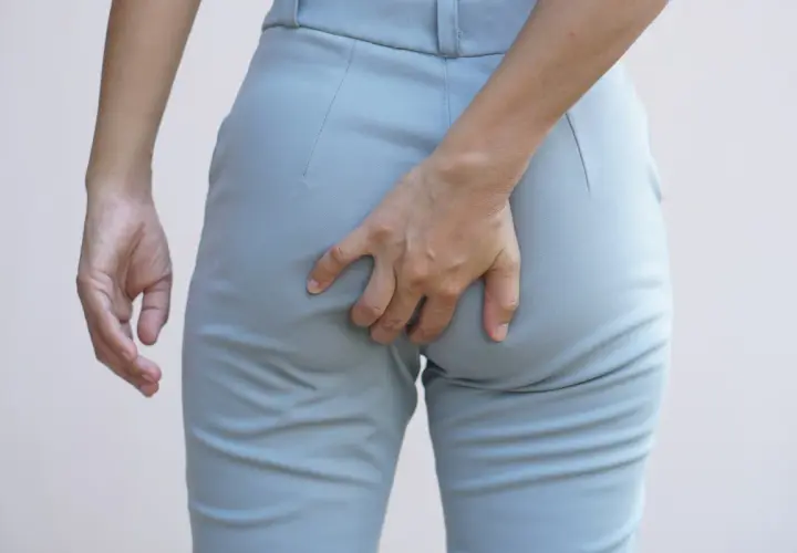 Mano che si gratta il **prurito fondoschiena** attraverso i pantaloni grigi.