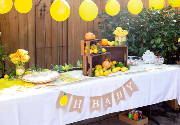 Udekorowany stół na baby shower z cytrynami, pomarańczami i żółtymi balonami.