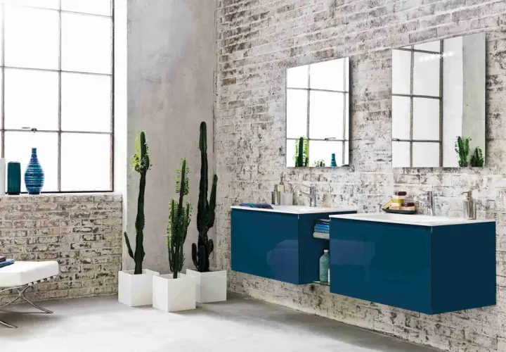 Bagno moderno con mattoni a vista, piante di cactus e mobili sospesi blu. Diversi tipi di piastrelle per un look industriale.