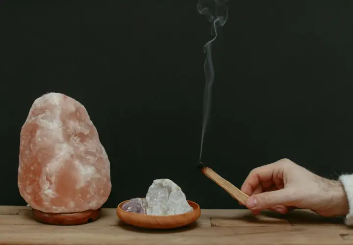 Lámpara de sal rosa, cristales y un palo de incienso humeante.