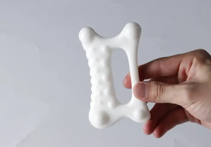 En hand håller ett vitt, benformat verktyg för gua sha massage kropp.