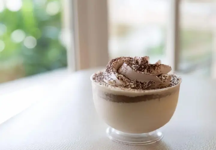 Delicioso mousse de café con crema batida y cacao espolvoreado, servido en un vaso transparente.