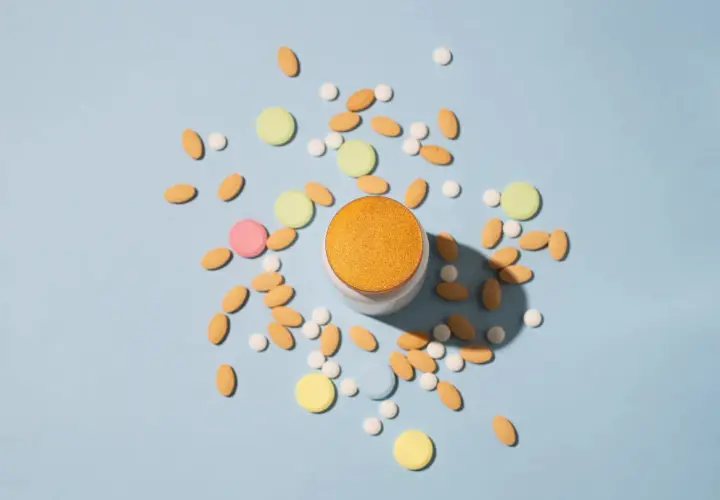 Pilules contraceptives et autres comprimés colorés dispersés autour d'un pot. Une solution pour l'acné ?
